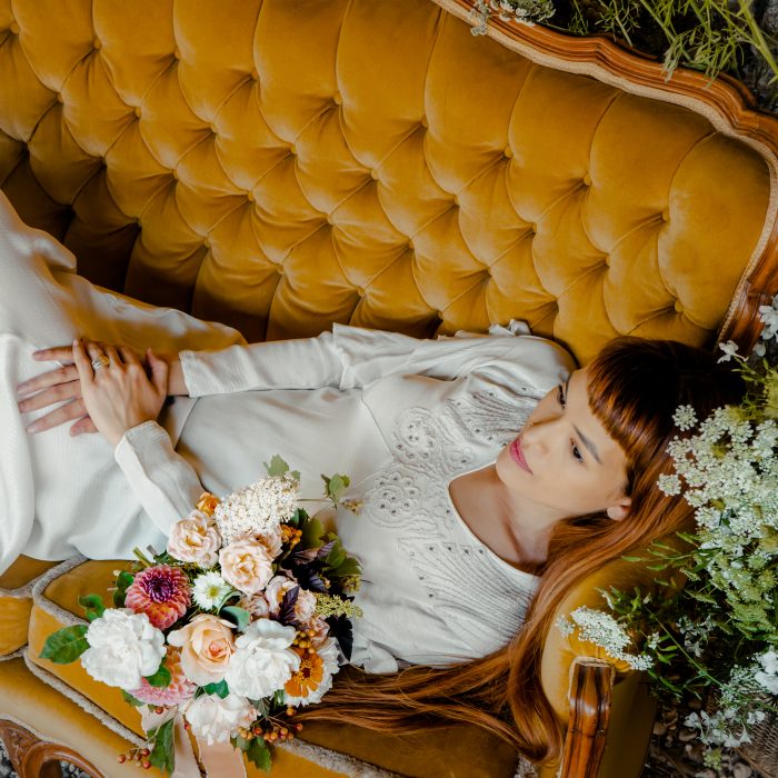 Bride lounging on an orange sofa with orange and white bouquet