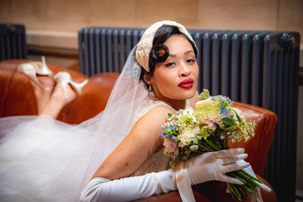 Glamorous bride holding bouquet, lounging on sofa at Cosy Club Bristol for a Dior wedding photoshoot